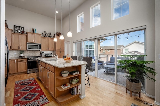 kitchen with a sink, light wood-style floors, appliances with stainless steel finishes, light stone countertops, and open shelves