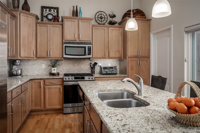 kitchen featuring tasteful backsplash, light wood-style flooring, appliances with stainless steel finishes, hanging light fixtures, and a sink