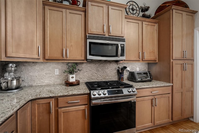 kitchen with a toaster, stainless steel appliances, tasteful backsplash, light stone countertops, and light wood-type flooring