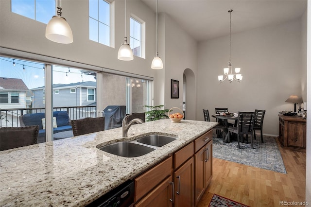 kitchen with arched walkways, light stone counters, light wood-style floors, pendant lighting, and a sink