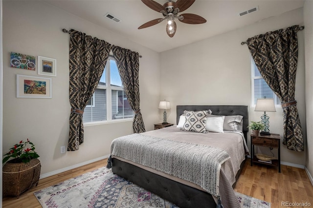 bedroom with a ceiling fan, visible vents, baseboards, and wood finished floors