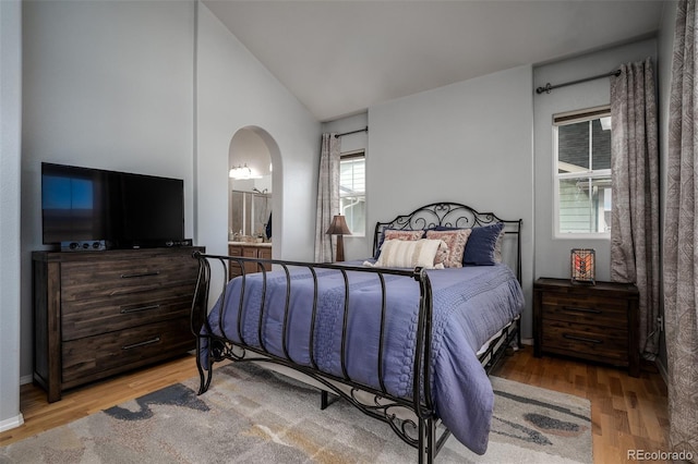 bedroom featuring arched walkways, vaulted ceiling, wood finished floors, and ensuite bathroom