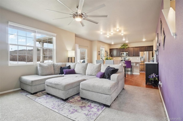 carpeted living area with baseboards and ceiling fan