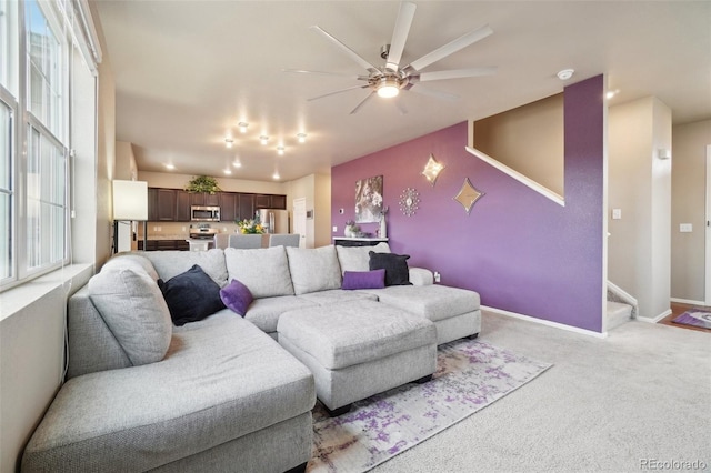 carpeted living area featuring stairs, baseboards, and ceiling fan