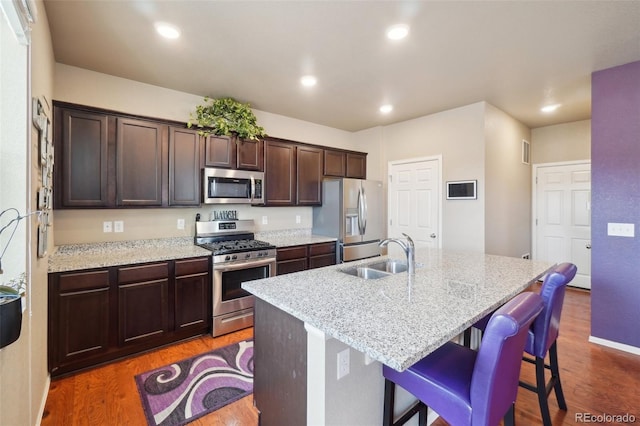 kitchen featuring a breakfast bar area, an island with sink, appliances with stainless steel finishes, wood finished floors, and a sink