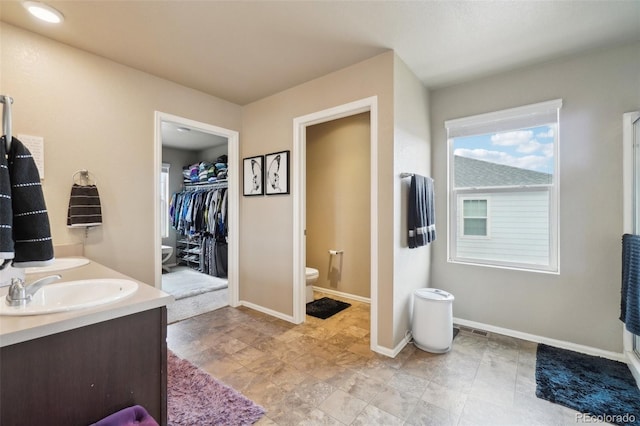 bathroom featuring a spacious closet, toilet, baseboards, and a sink