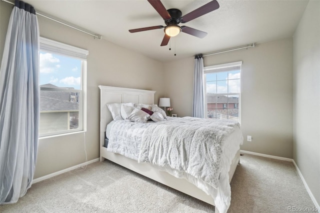 bedroom featuring ceiling fan, multiple windows, baseboards, and light carpet