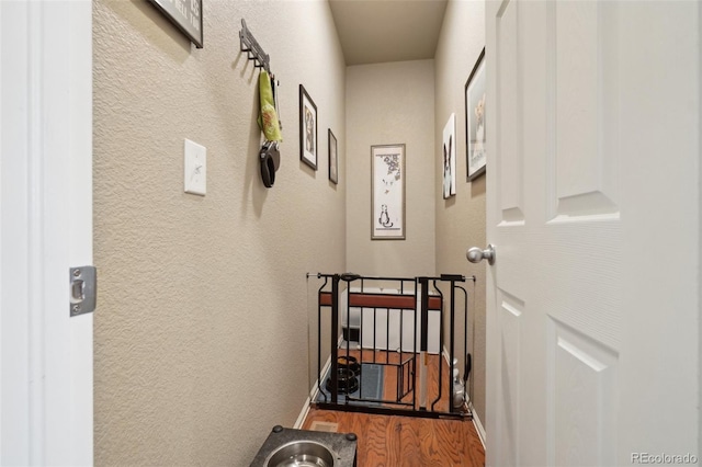 corridor featuring wood finished floors, baseboards, and a textured wall