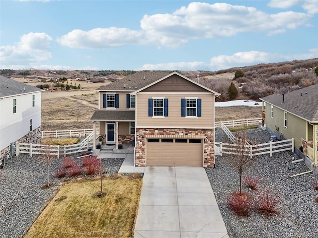 view of front of house featuring stone siding, concrete driveway, a garage, and fence