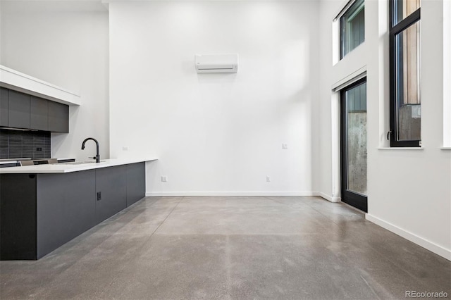 unfurnished living room featuring a towering ceiling, a wall unit AC, and sink