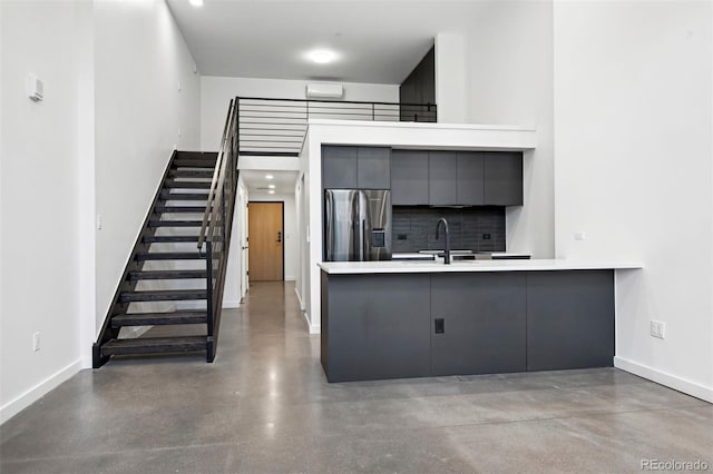 kitchen featuring gray cabinetry, backsplash, kitchen peninsula, stainless steel fridge, and concrete flooring