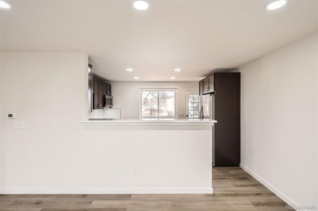 kitchen featuring tasteful backsplash, kitchen peninsula, light hardwood / wood-style floors, and dark brown cabinets