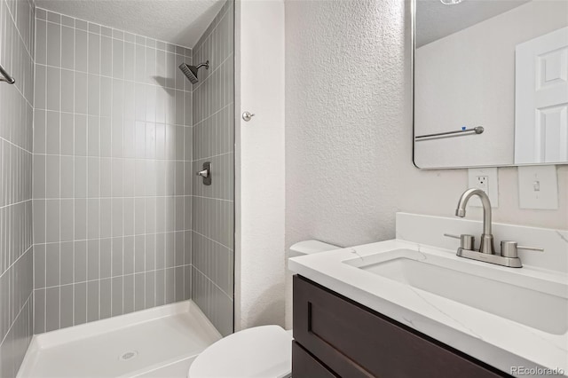 bathroom featuring vanity, toilet, a textured ceiling, and a tile shower