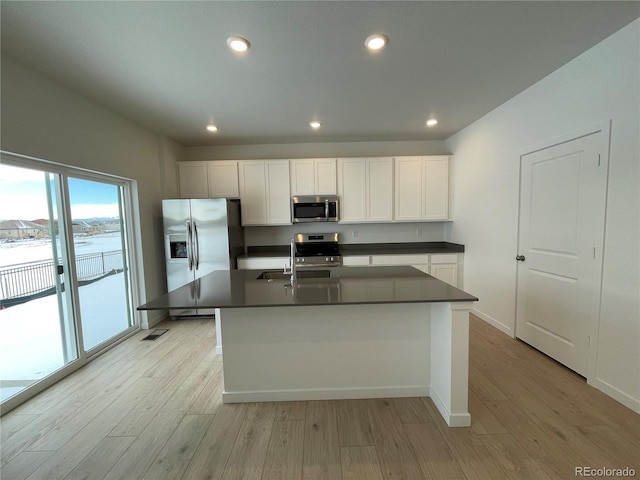 kitchen featuring stainless steel appliances, an island with sink, white cabinets, and light hardwood / wood-style flooring