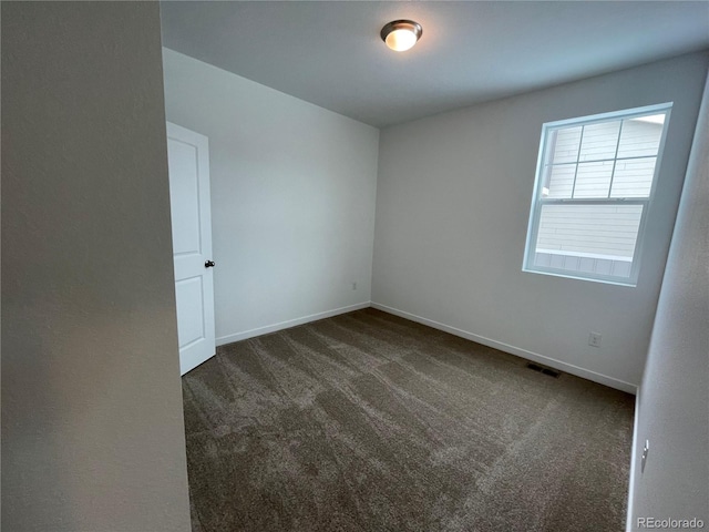 unfurnished room with visible vents, dark carpet, and baseboards