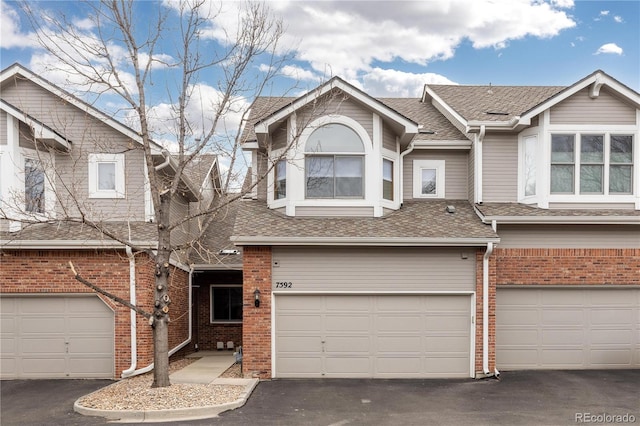 view of property with roof with shingles, an attached garage, brick siding, and aphalt driveway