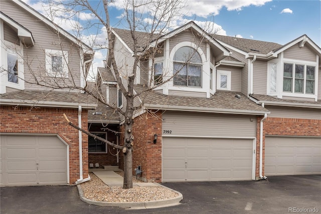 view of property featuring an attached garage, brick siding, and aphalt driveway