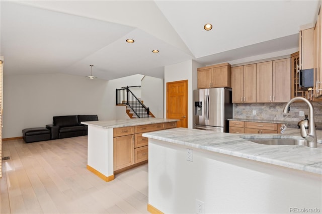 kitchen with light countertops, a sink, a peninsula, lofted ceiling, and stainless steel refrigerator with ice dispenser