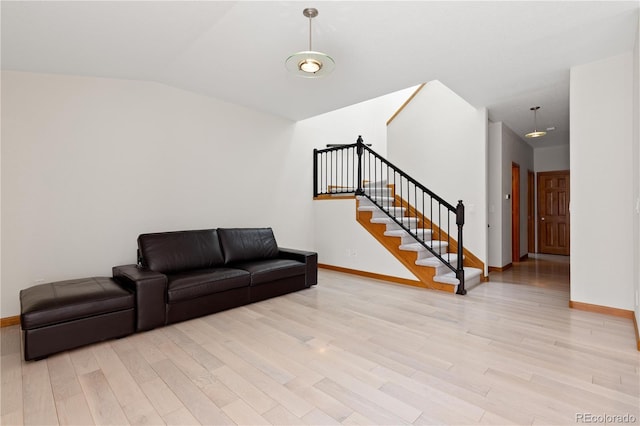 living area with lofted ceiling, baseboards, light wood-style floors, and stairs