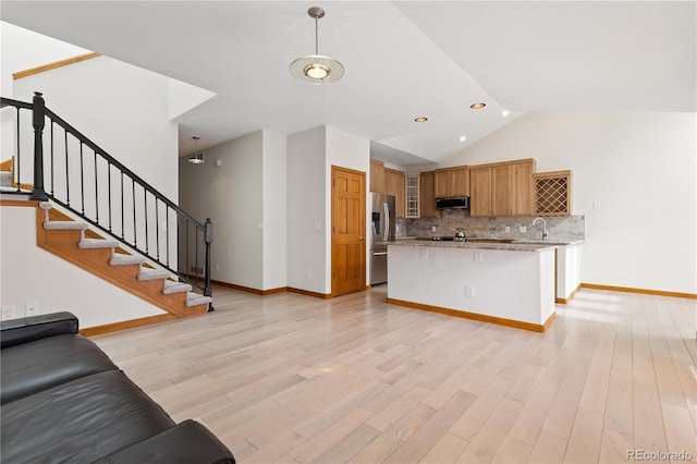 kitchen featuring open floor plan, tasteful backsplash, light wood-type flooring, a sink, and appliances with stainless steel finishes