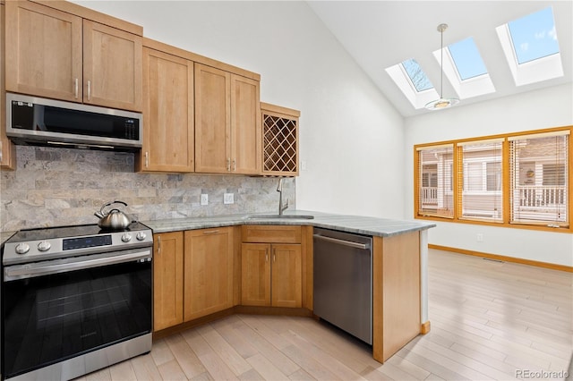 kitchen with tasteful backsplash, a sink, vaulted ceiling with skylight, a peninsula, and appliances with stainless steel finishes