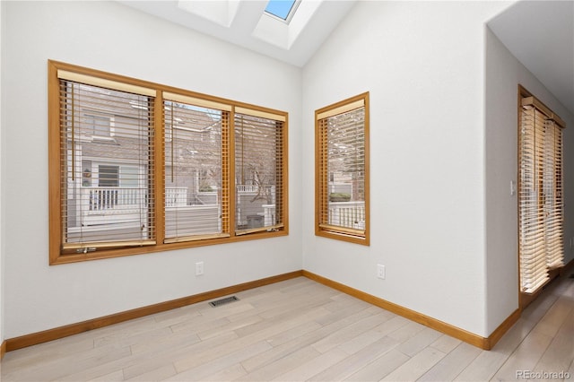 spare room featuring baseboards, visible vents, lofted ceiling with skylight, and light wood-type flooring