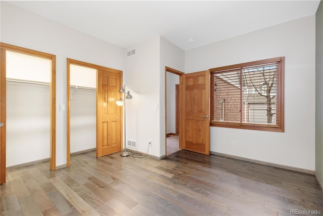 unfurnished bedroom featuring two closets, wood finished floors, and visible vents