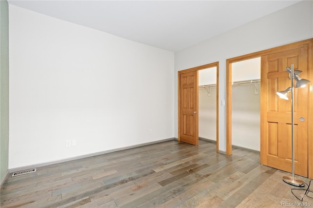 unfurnished bedroom featuring baseboards, visible vents, light wood-style floors, and two closets