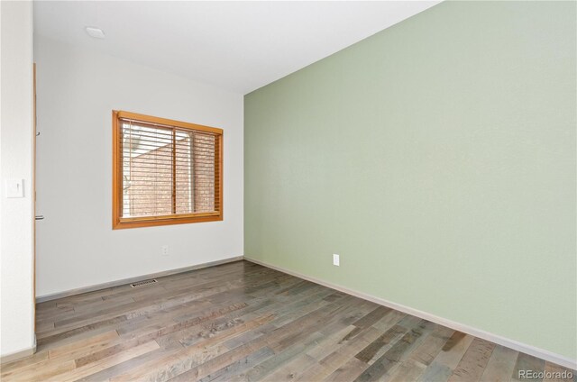 unfurnished room featuring baseboards, visible vents, and wood finished floors