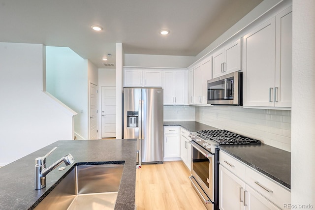 kitchen featuring sink, light hardwood / wood-style flooring, appliances with stainless steel finishes, white cabinets, and backsplash