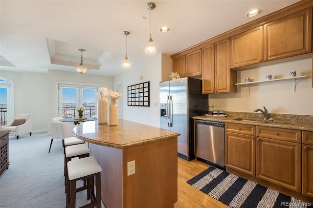 kitchen featuring stainless steel appliances, a raised ceiling, a center island, decorative light fixtures, and sink