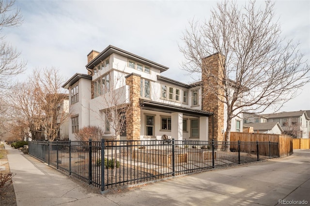 view of front of property featuring stone siding, a fenced front yard, a chimney, and stucco siding