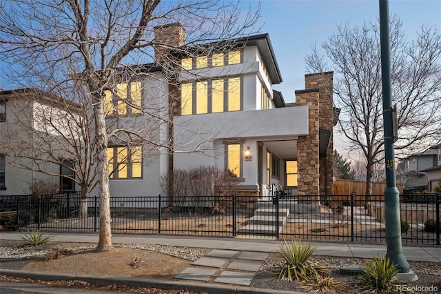 contemporary house with a fenced front yard, a chimney, and stucco siding