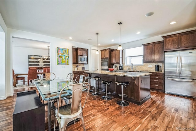 kitchen featuring hanging light fixtures, a kitchen island, light stone countertops, built in appliances, and a kitchen bar