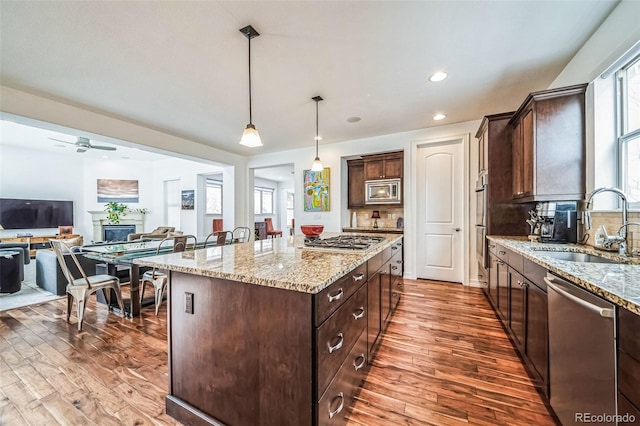 kitchen featuring a sink, hanging light fixtures, appliances with stainless steel finishes, dark brown cabinets, and a center island