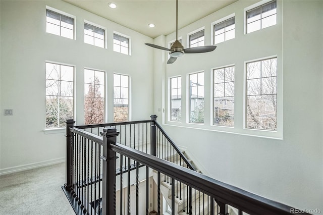 hall featuring a towering ceiling, recessed lighting, baseboards, and an upstairs landing