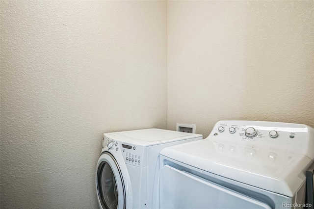 washroom with a textured wall, laundry area, and washing machine and clothes dryer