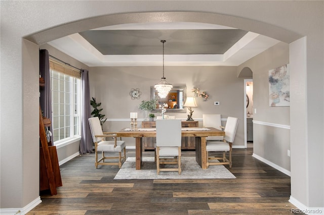 dining area with a raised ceiling, dark wood-type flooring, and an inviting chandelier