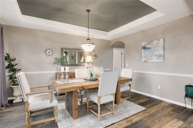 dining space featuring an inviting chandelier, dark hardwood / wood-style floors, and a raised ceiling