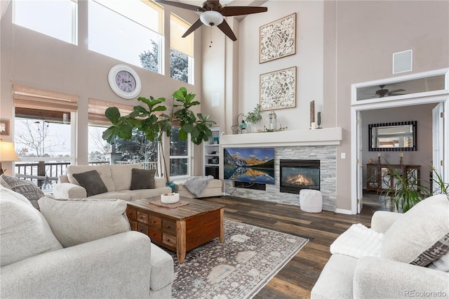 living room featuring plenty of natural light, dark hardwood / wood-style floors, a stone fireplace, and a high ceiling