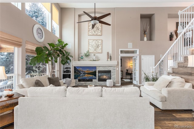 living room featuring a stone fireplace, ceiling fan, dark wood-type flooring, and a high ceiling