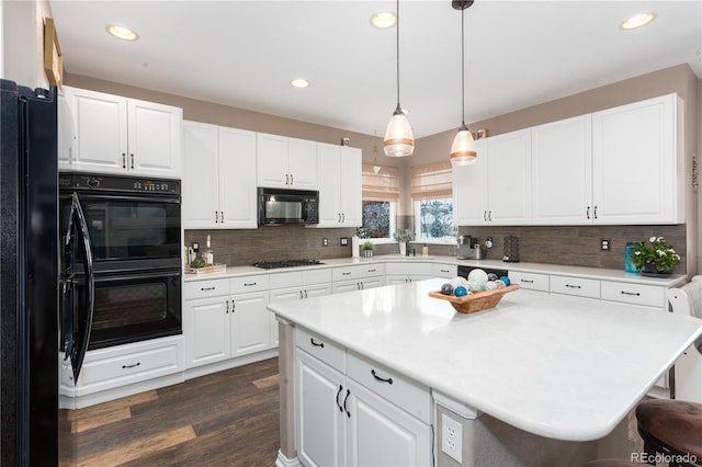 kitchen featuring decorative light fixtures, white cabinetry, a kitchen island, and black appliances