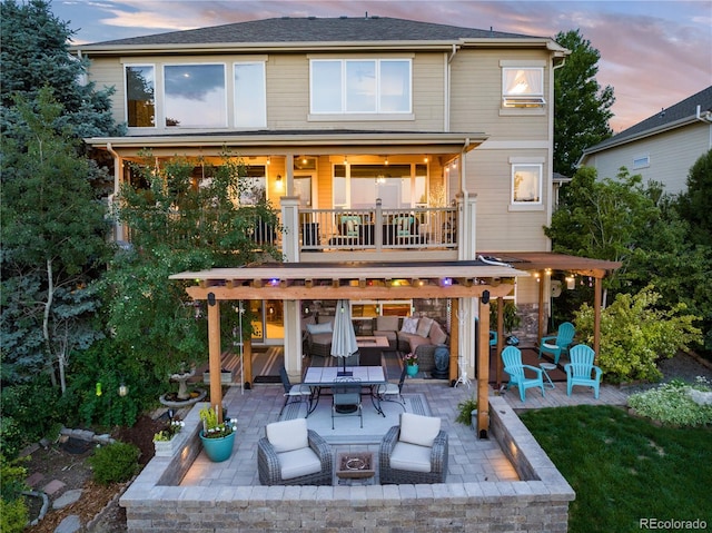 back house at dusk featuring a patio, a balcony, and a fire pit