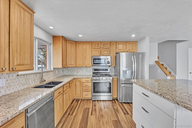 kitchen featuring light wood-type flooring, backsplash, light stone countertops, appliances with stainless steel finishes, and a sink