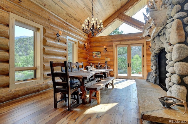 dining area with hardwood / wood-style floors, a notable chandelier, vaulted ceiling with beams, rustic walls, and a stone fireplace