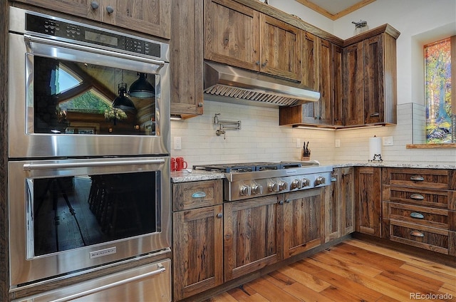 kitchen featuring light stone countertops, light hardwood / wood-style flooring, appliances with stainless steel finishes, ornamental molding, and decorative backsplash