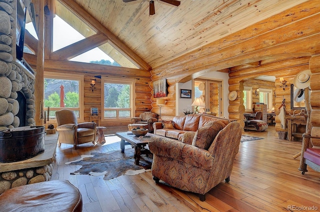 living room with hardwood / wood-style floors, a stone fireplace, high vaulted ceiling, ceiling fan, and rustic walls