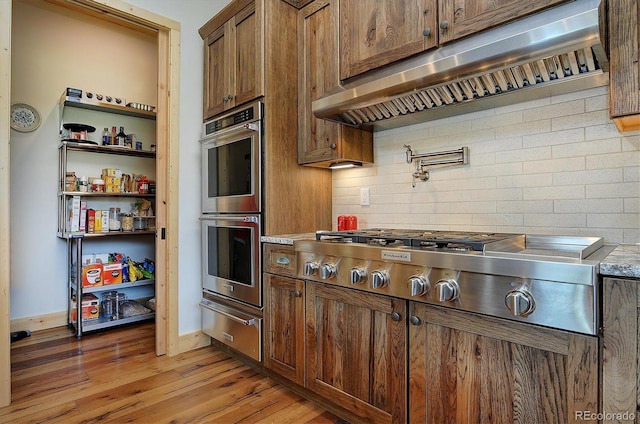 kitchen with range hood, decorative backsplash, stainless steel appliances, and light hardwood / wood-style floors