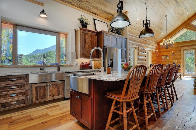 kitchen with an inviting chandelier, light stone countertops, decorative light fixtures, an island with sink, and sink