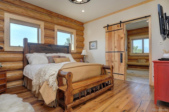 bedroom with a barn door, wood-type flooring, and rustic walls